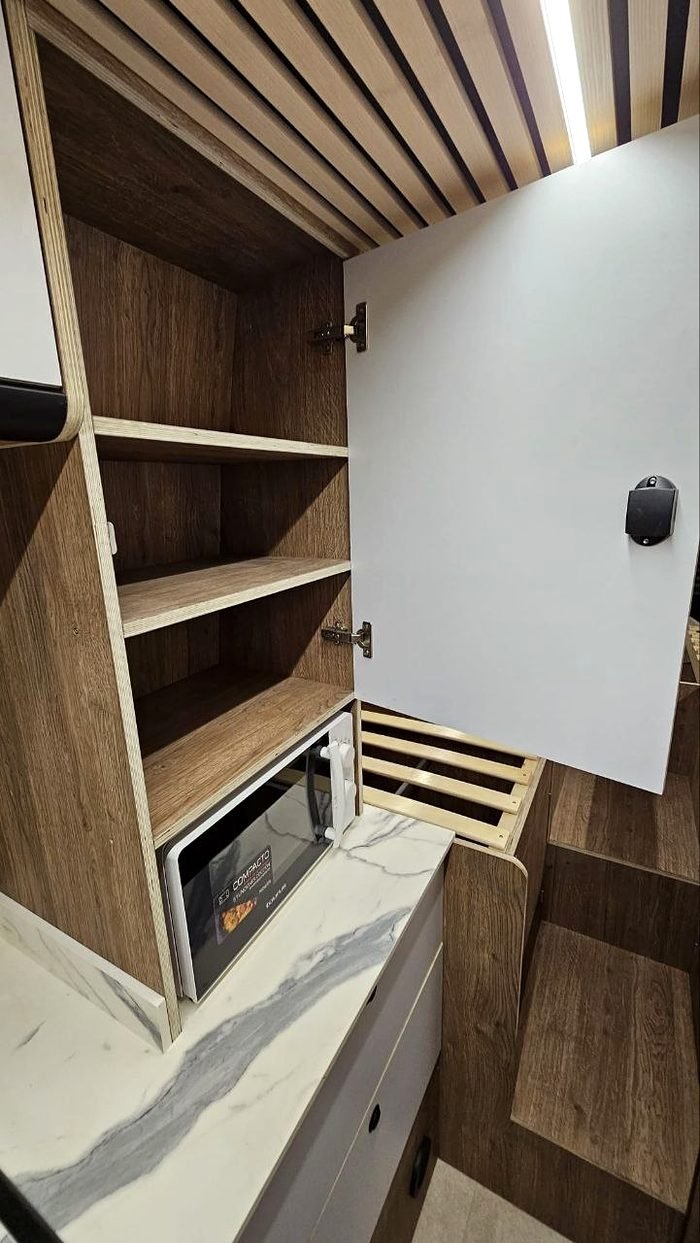Armario abierto de una camper con microondas integrado y baldas de madera