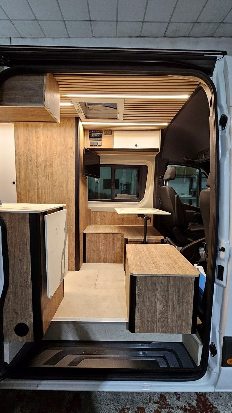 Interior de una camper con mobiliario de madera, mesa y banco corrido